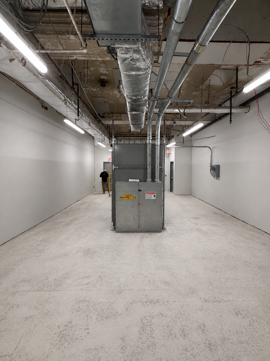 Completed basement equipment room, painted white walls, clean concrete floor, existing electrical equipment and ductwork in place.